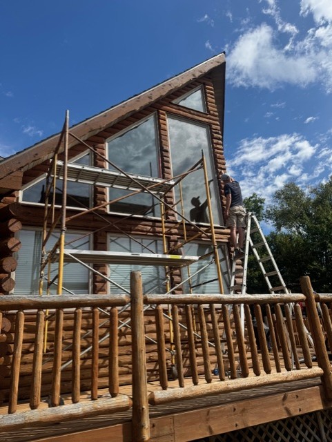 Exterior work around a log cabin’s tall windows and timber deck