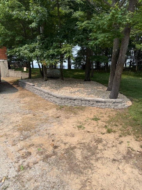 After landscaping: curved block retaining wall with a stone bed around the trees beside the driveway